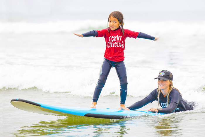 Instructor helping girl ride surfboard at Corky Carroll's Surf Camp in Huntington Beach