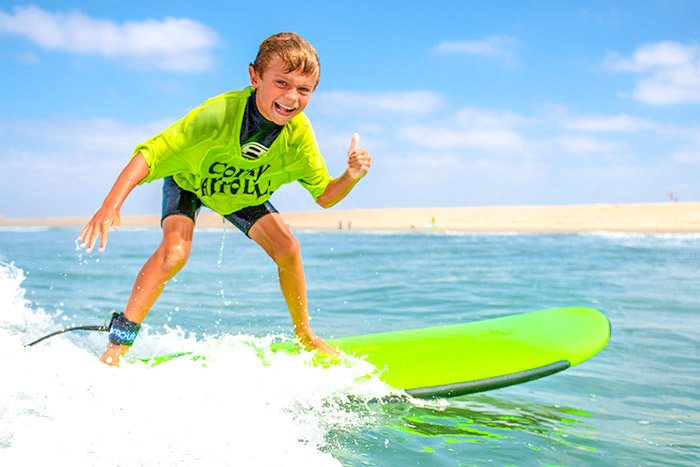 Smiling camper riding surfboard giving thumbs up at Corky Carroll's Surf Camp in Huntington Beach